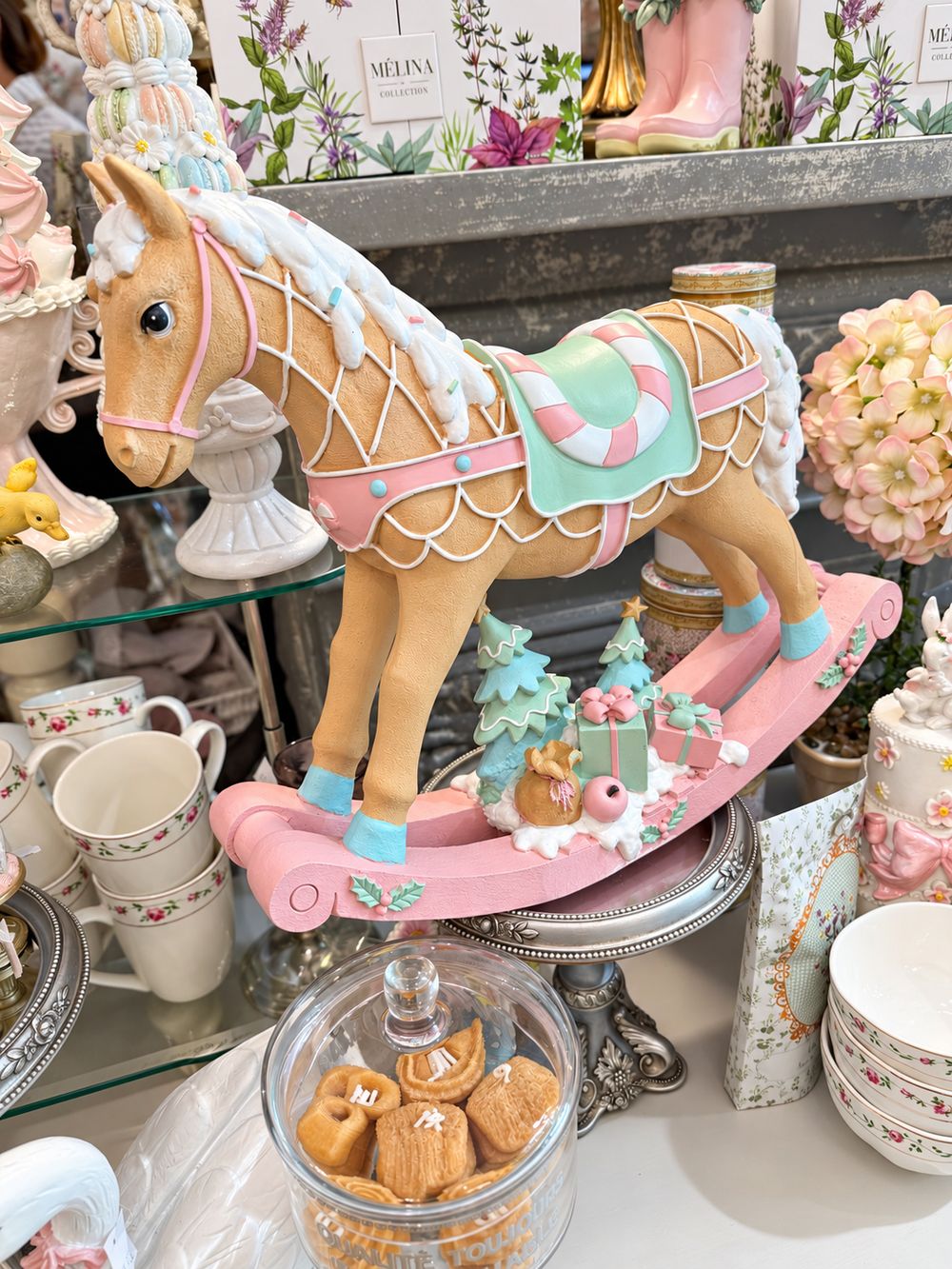 Grand cheval à bascule décoratif aux tons rose pastel, vert menthe, blanc et caramel, dans un style féérique et gourmand pour une décoration de Noël poétique.