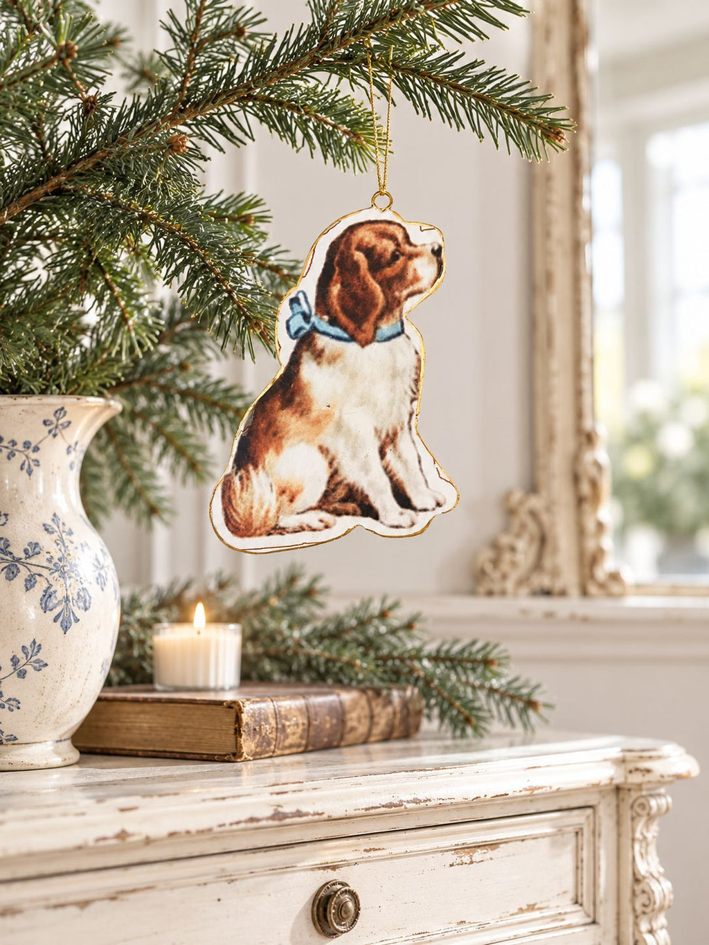 Suspension chien victorien sur une branche de sapin au-dessus d’une console ancienne, près d’un vase et d’un miroir.