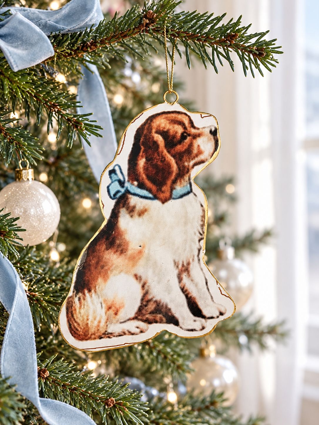 Suspension chien victorien accrochée dans un sapin décoré de boules nacrées et de rubans bleu pâle.