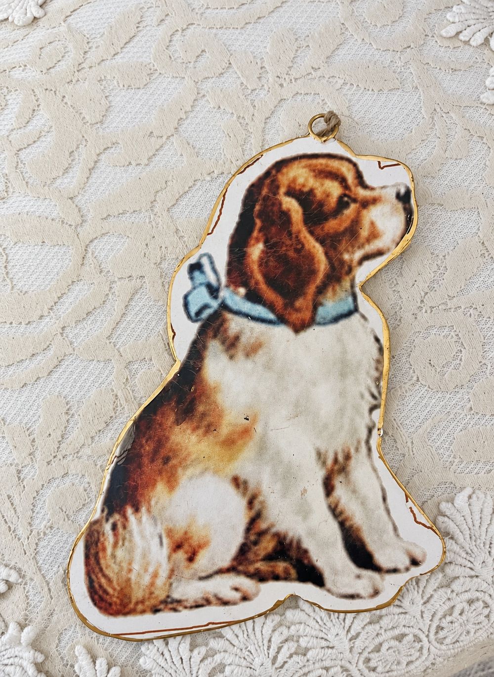 Suspension chien victorien en métal imprimé, posée sur une dentelle crème.