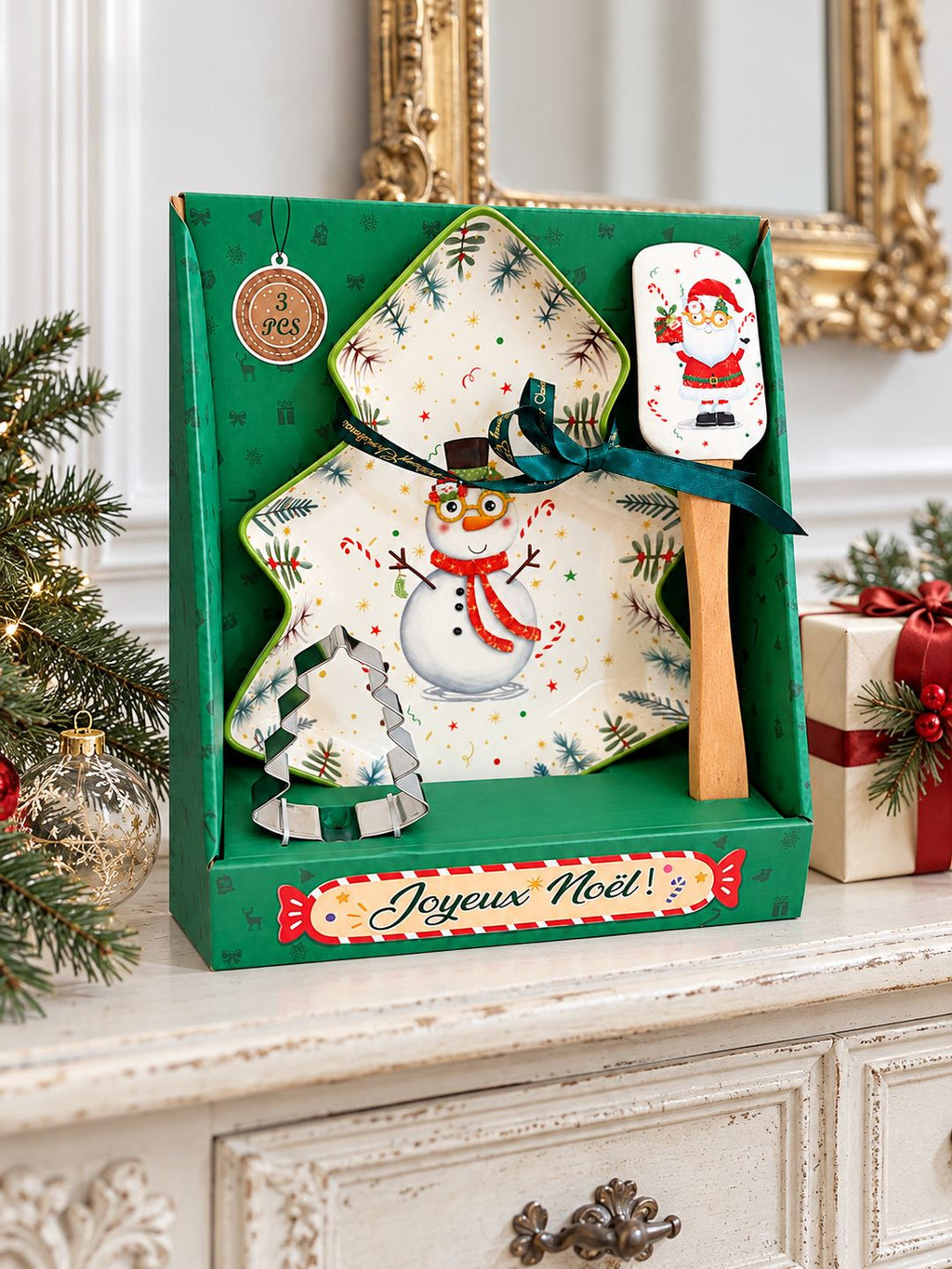 Coffret Snowman de Noël sur une console patinée, accompagné d’un cadeau et de branches de sapin.