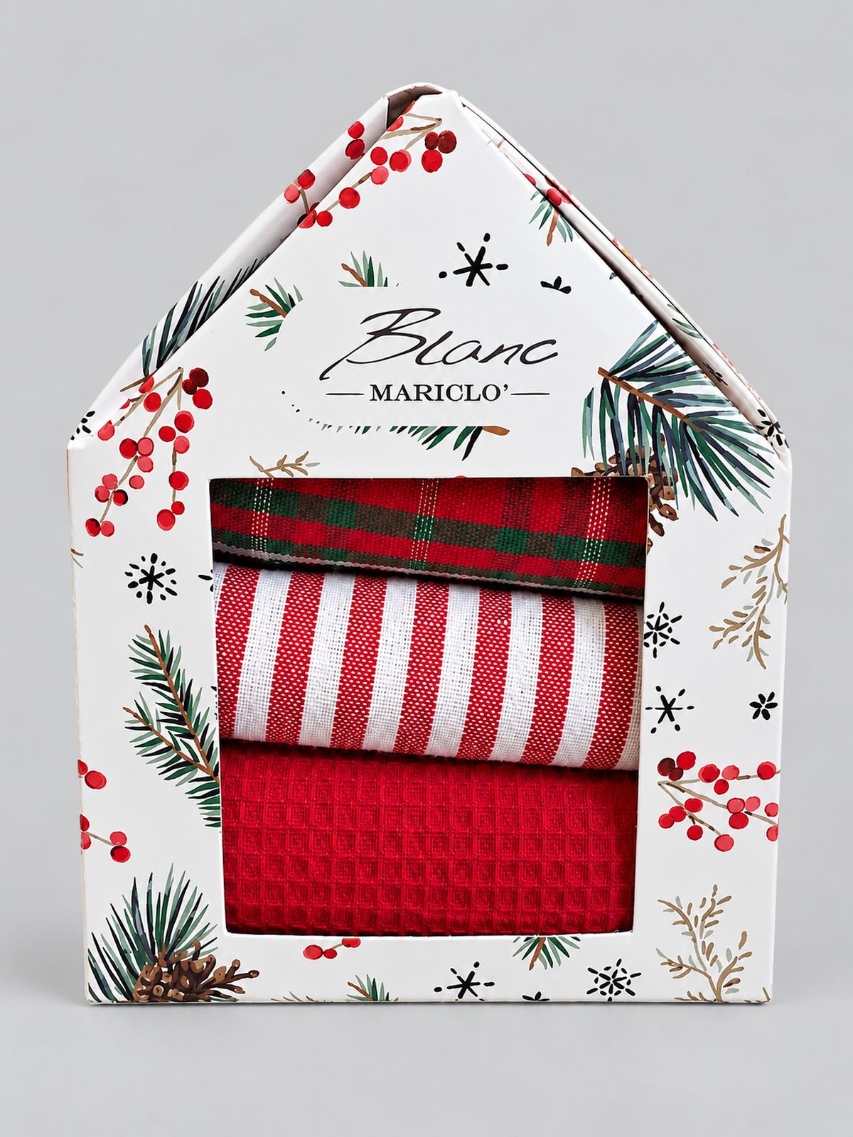 Coffret de trois torchons de Noël Blanc MariClò dans une boîte maisonnette à motifs de sapin et de baies rouges, sur fond gris clair.