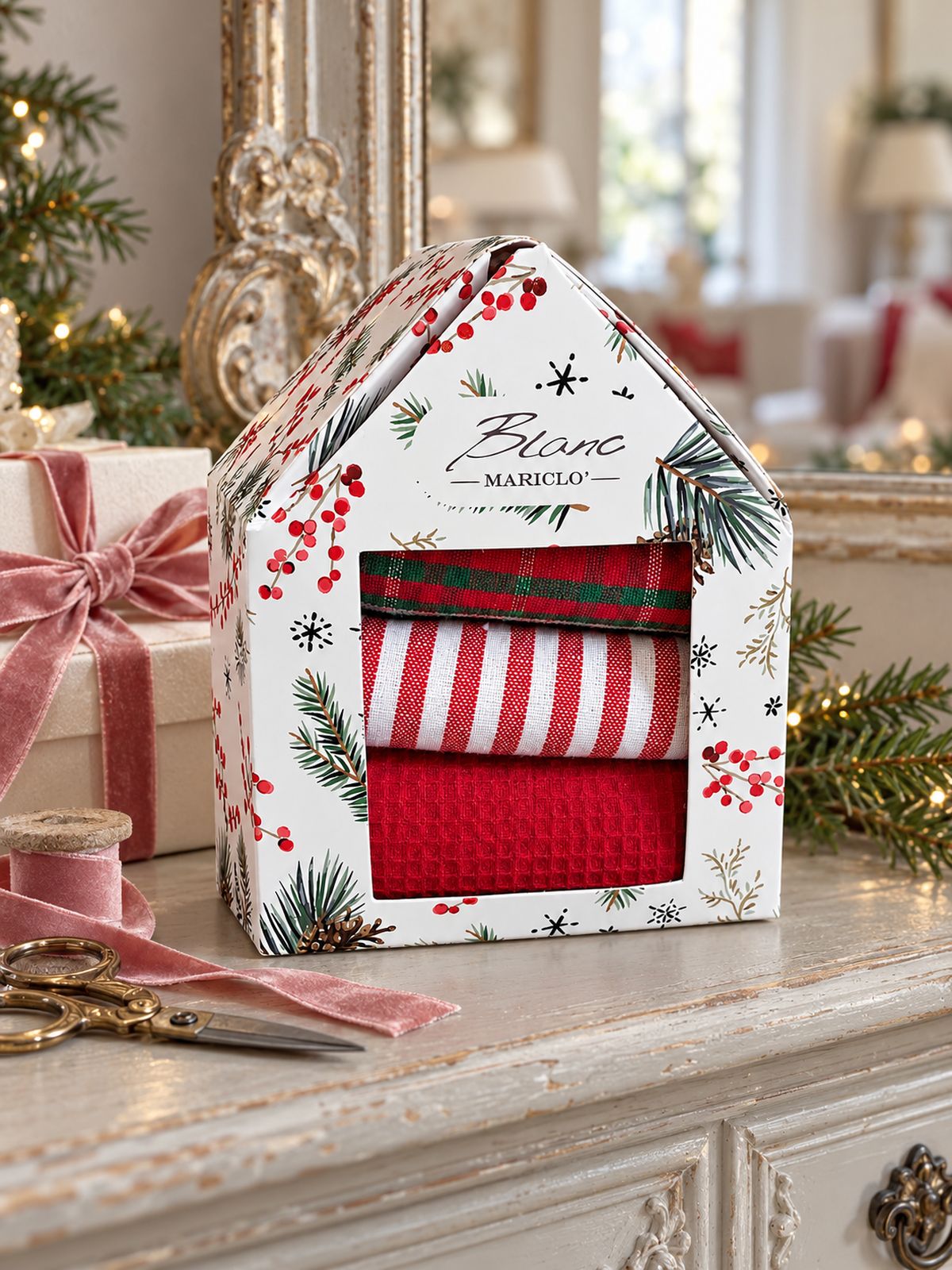 Coffret de torchons de Noël Blanc MariClò sur une console patinée, accompagné d’un cadeau et d’un ruban vieux rose.
