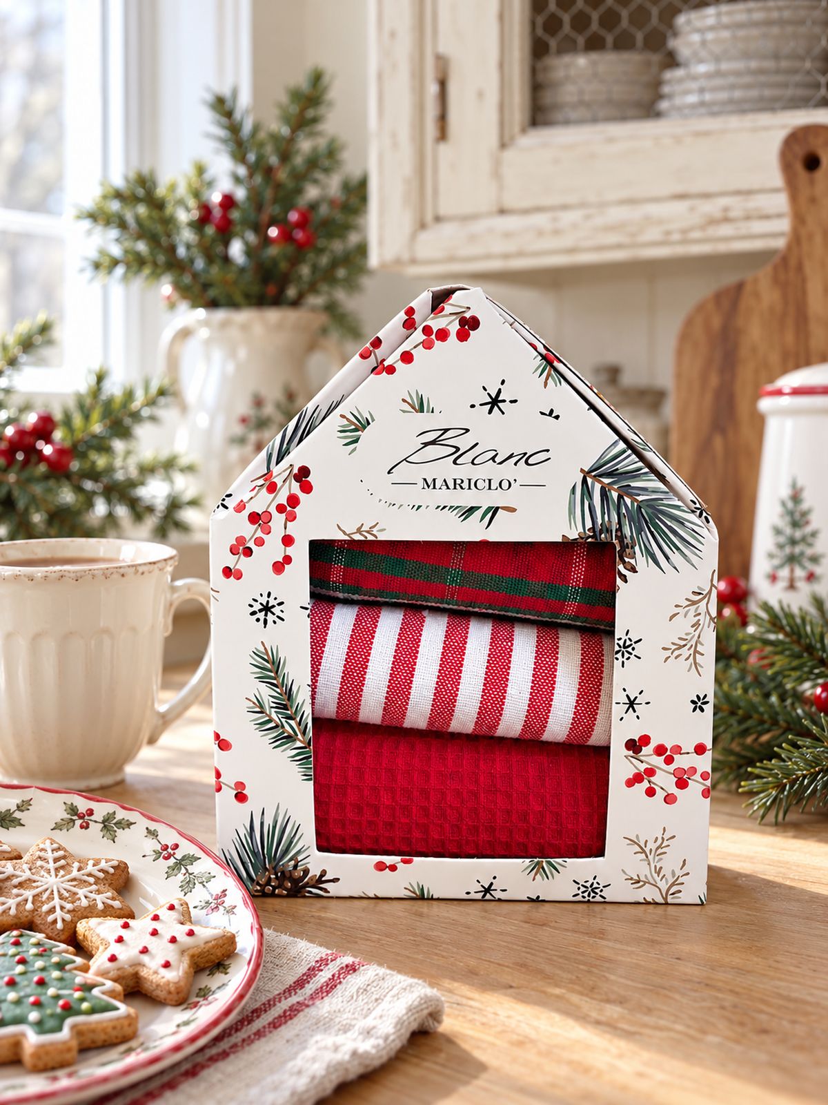 Coffret de torchons de Noël Blanc MariClò sur un plan de travail en bois clair, près d’une tasse et de biscuits décorés.
