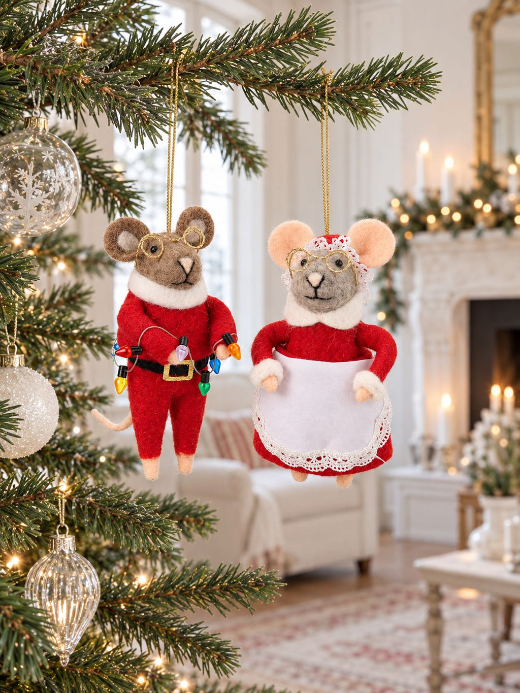 Couple de souris de Noël suspendues au sapin, dans un salon lumineux avec cheminée ancienne et décorations de Noël.