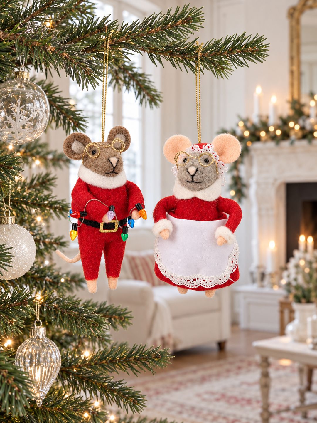 Couple de souris de Noël suspendues au sapin, dans un salon lumineux avec cheminée ancienne et décorations de Noël.