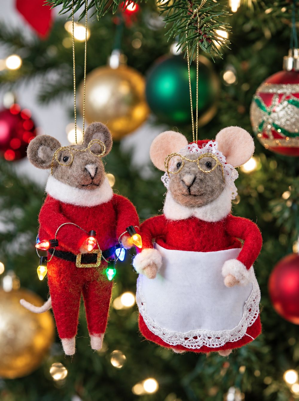 Couple de souris en feutrine suspendues dans un sapin de Noël, avec lunettes dorées et petites ampoules colorées.