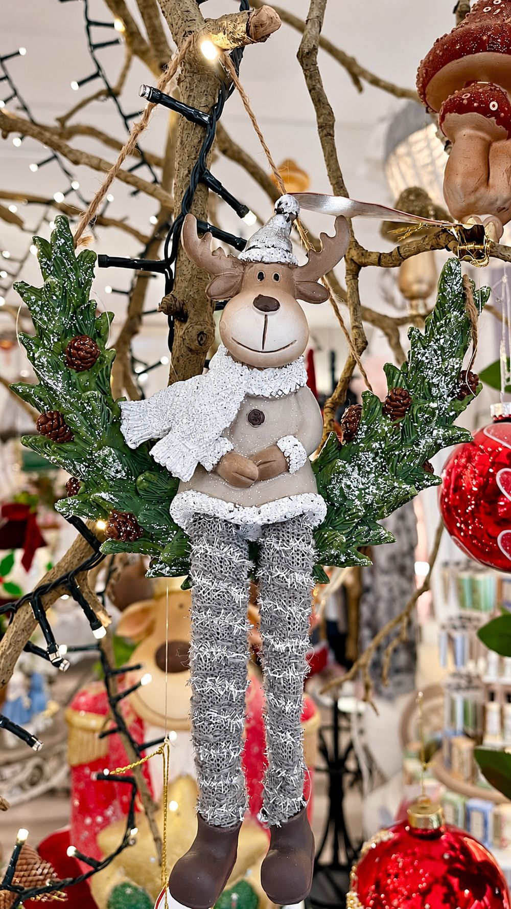 Couronne Renne d’Hiver avec écharpe blanche et jambes argentées, suspendue parmi les décorations de Noël.