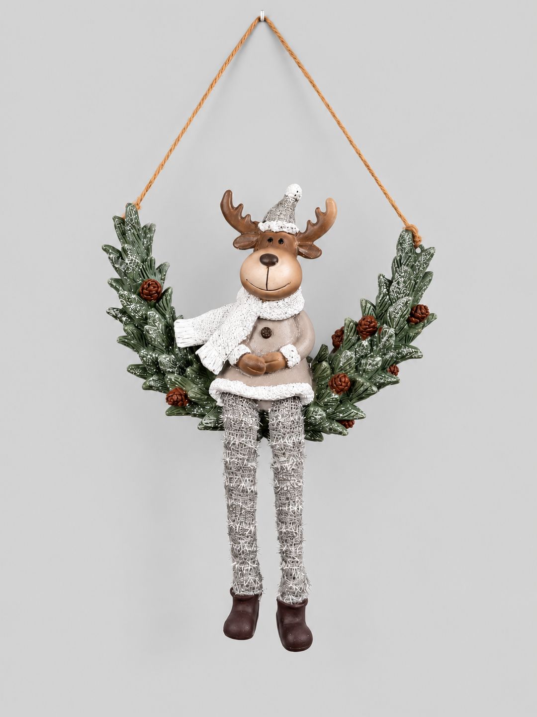 Couronne Renne d’Hiver à suspendre, avec feuillage givré, pommes de pin et longues jambes argentées, sur fond gris clair.