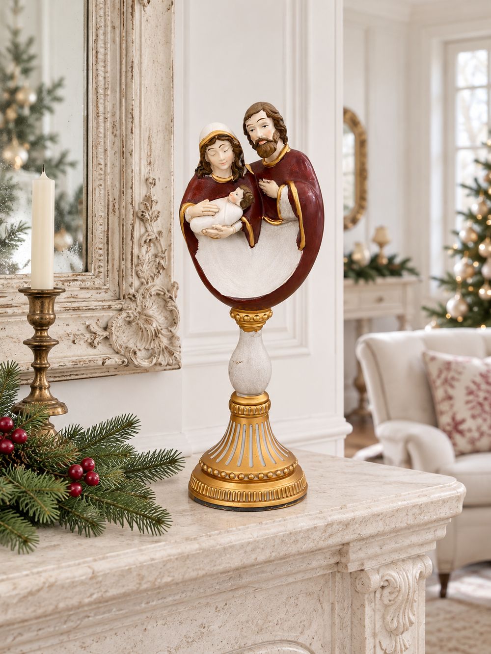 Crèche sur socle baroque doré posée sur une cheminée claire, près d’un chandelier et de branches de sapin.