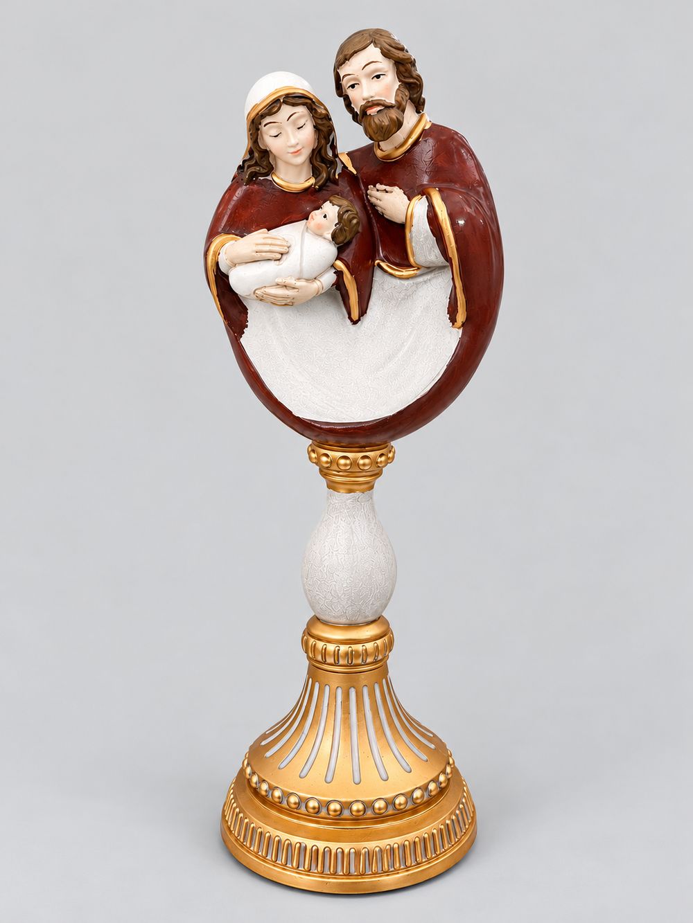 Crèche de la Sainte Famille aux tons bordeaux et ivoire sur un socle baroque doré, sur fond gris clair.