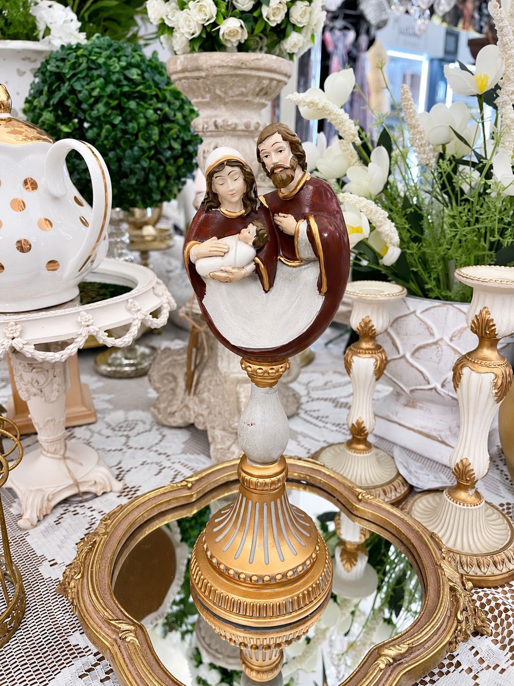 Crèche de la Sainte Famille aux tons bordeaux et ivoire sur un socle baroque doré, vue de face.