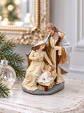 Crèche de Noël sur une console blanche patinée, près d’une boule de verre et d’une branche de sapin.