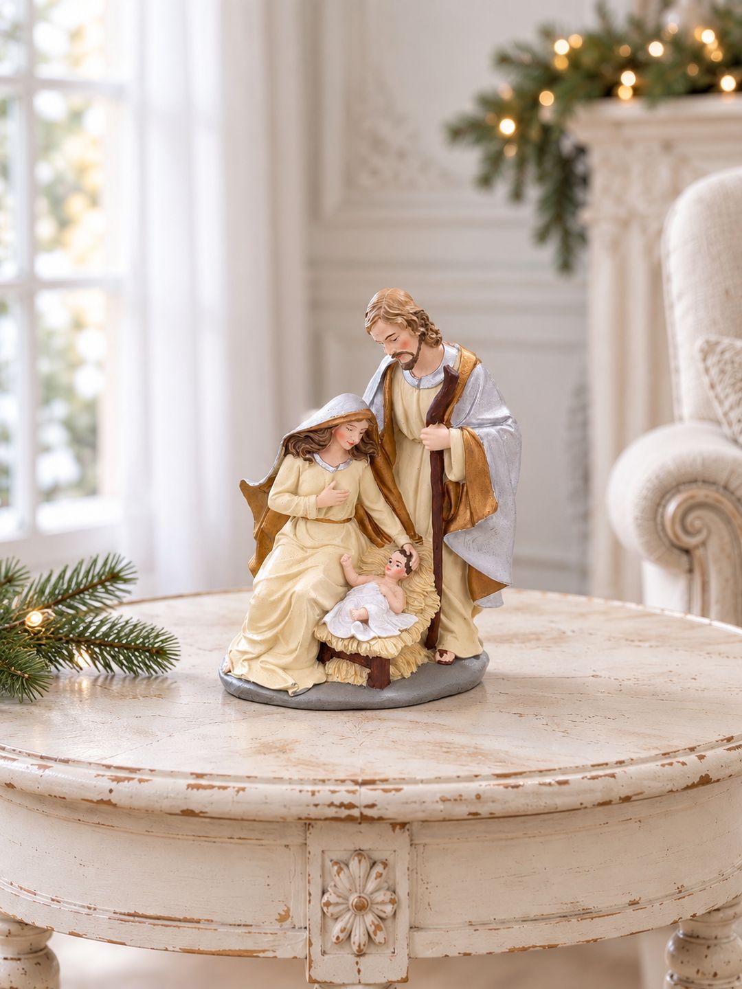 Crèche de Noël sur une table ronde patinée dans un salon lumineux, près d’un fauteuil en lin.