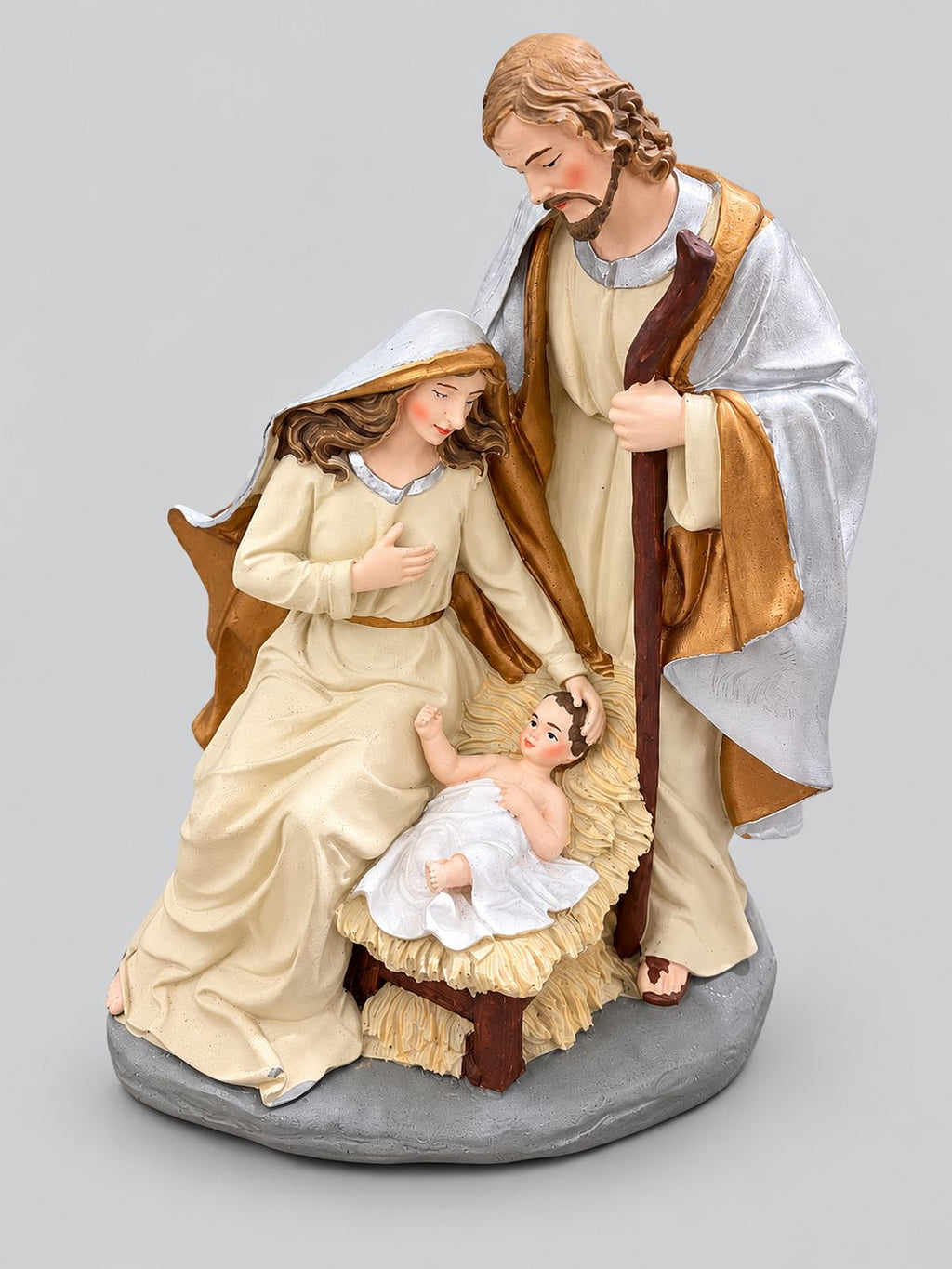 Crèche de Noël en résine crème, dorée et argentée représentant Marie, Joseph et l’enfant Jésus, sur fond gris clair.