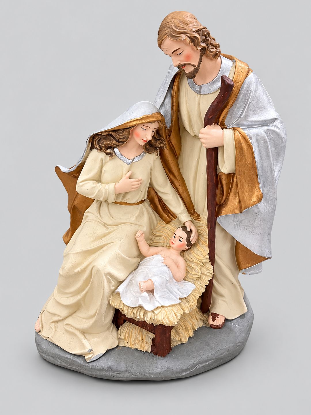Crèche de Noël en résine crème, dorée et argentée représentant Marie, Joseph et l’enfant Jésus, sur fond gris clair.