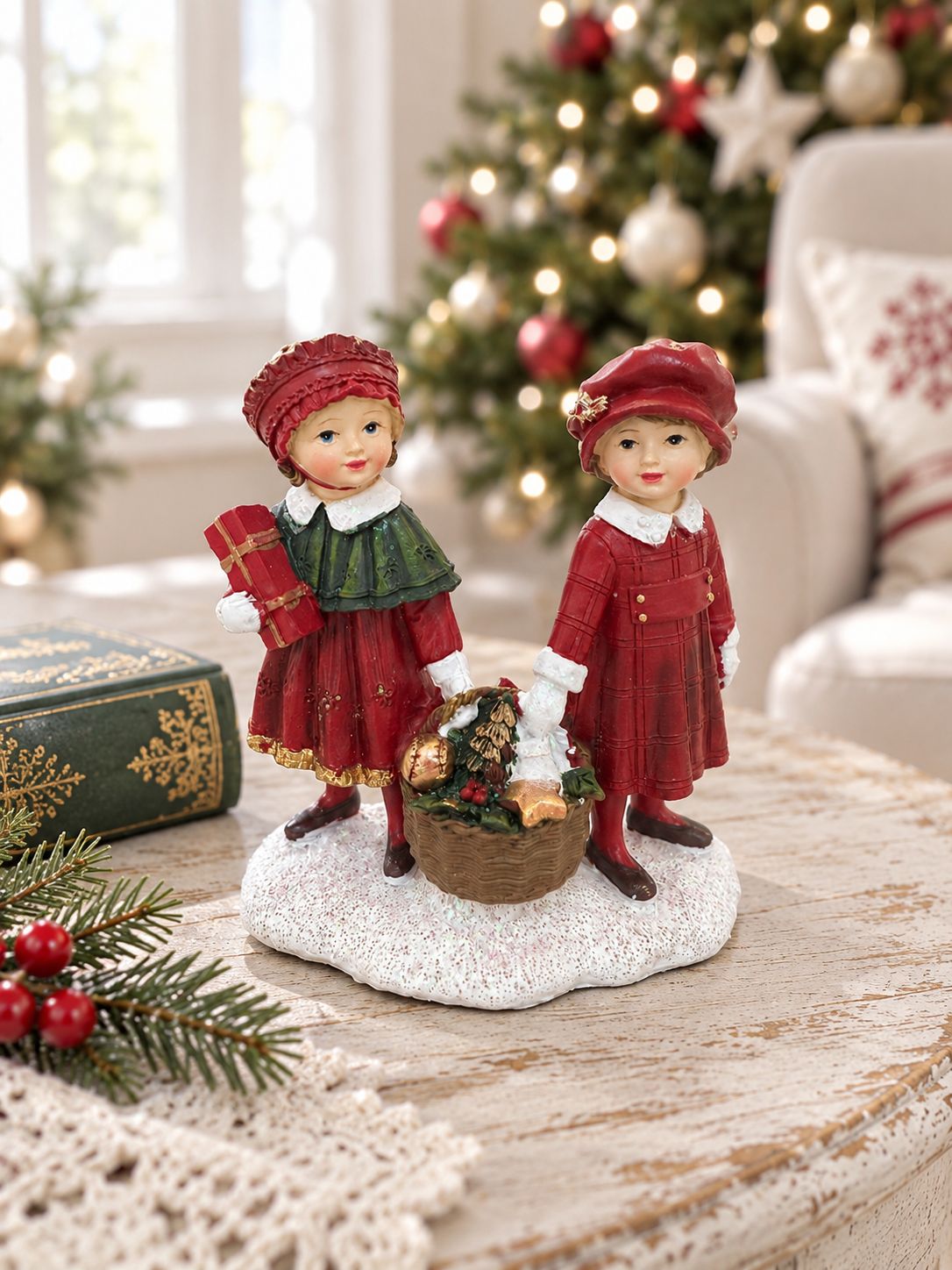 Figurine Enfants au Panier de Noël sur une table patinée, avec un livre ancien et un sapin dans un salon lumineux.