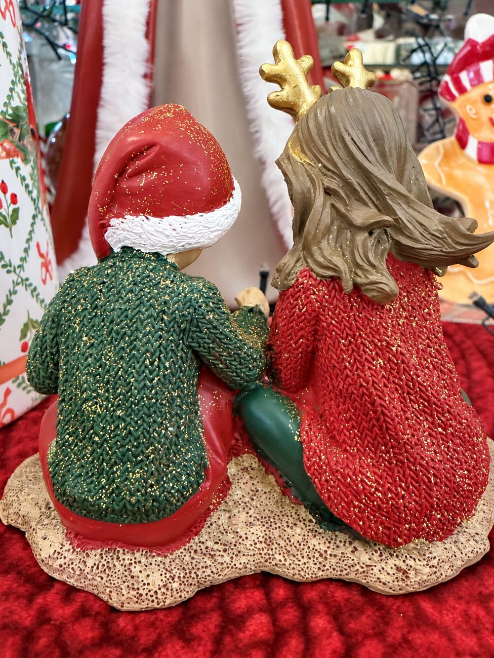 Vue de dos des Enfants au Trésor de Noël, avec les cheveux sculptés, le bonnet rouge et les vêtements à paillettes.