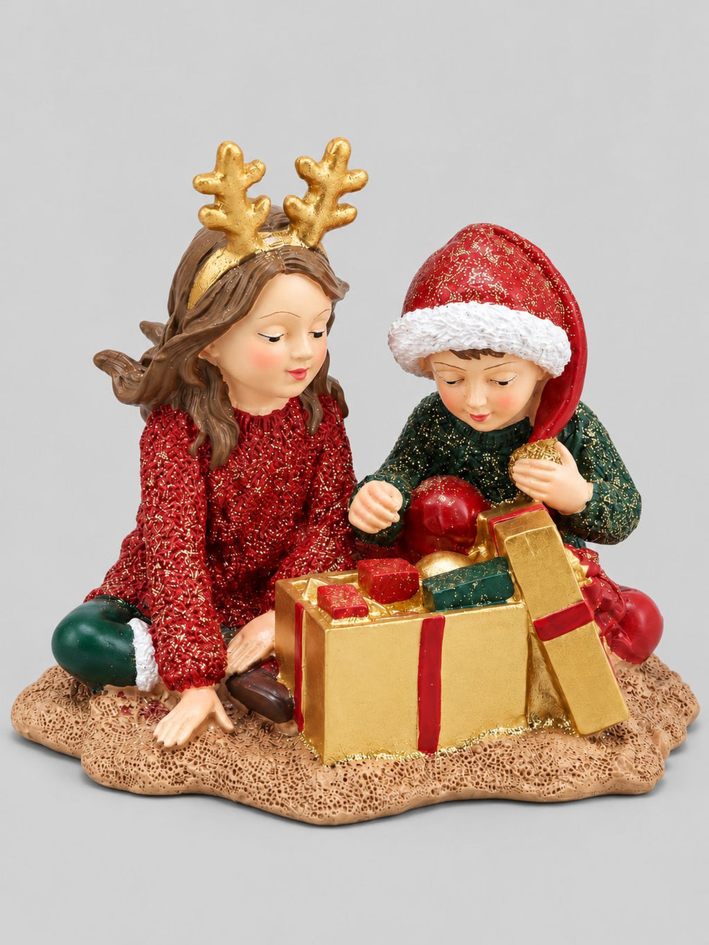 Figurine Les Enfants au Trésor de Noël, deux enfants en tenues rouge et verte autour d’un cadeau doré ouvert, sur fond gris clair.