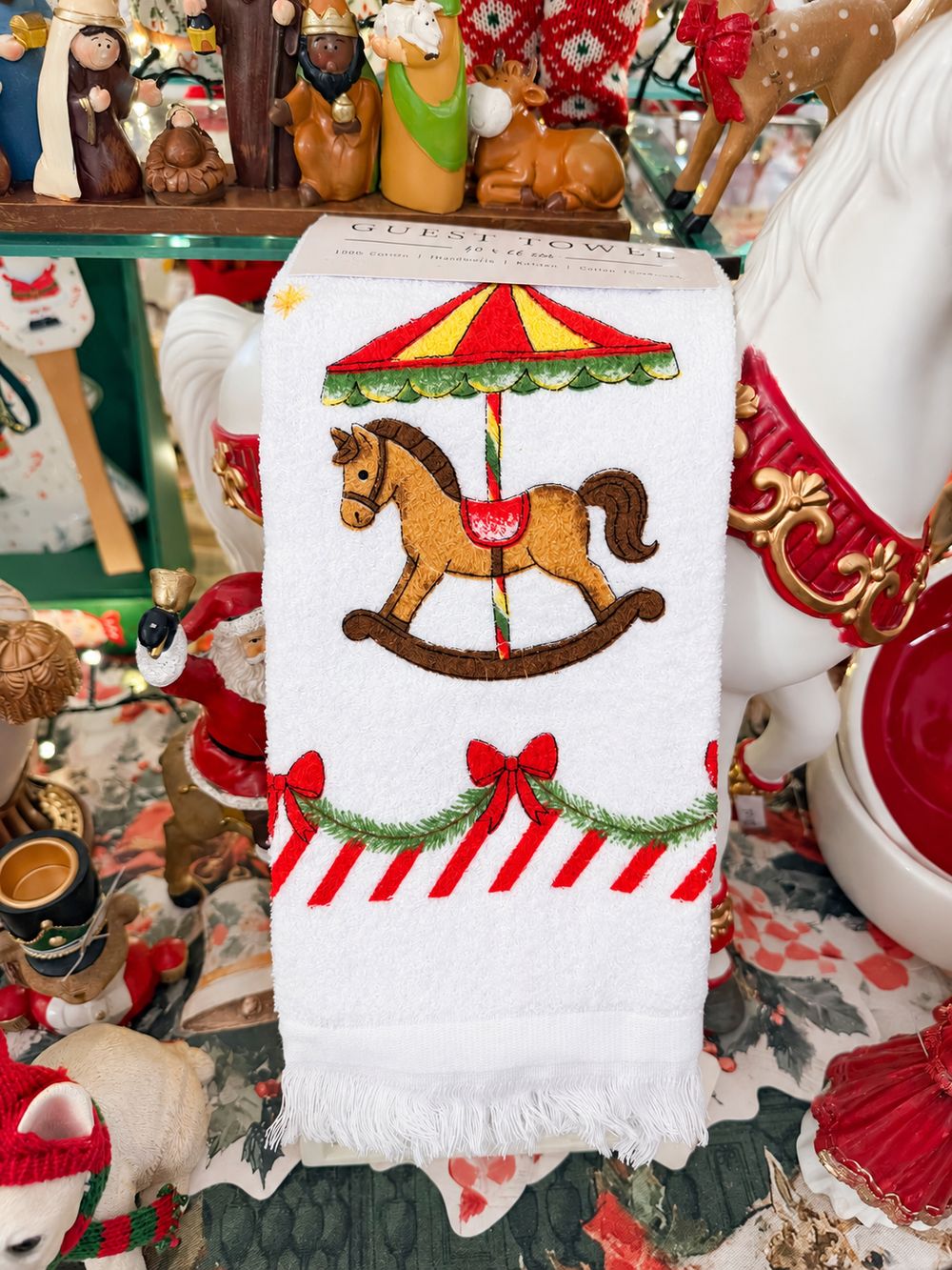 Essuie-main Carrousel de Noël blanc à franges, présenté plié dans le décor de la boutique, vue 2.