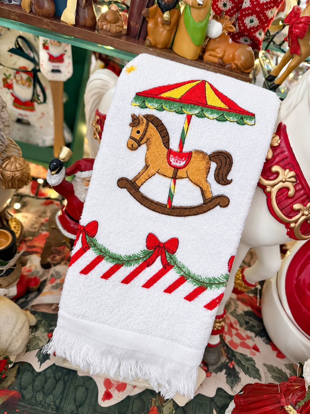 Essuie-main Carrousel de Noël blanc à franges, présenté plié dans le décor de la boutique, vue 3.