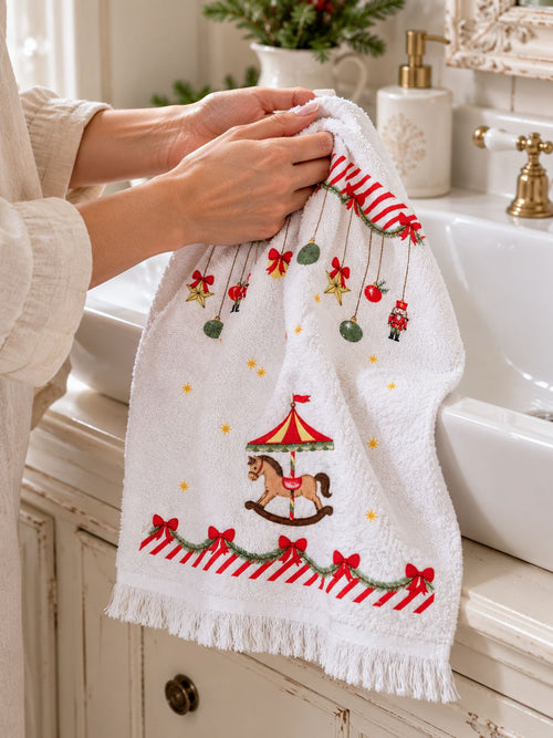 Mains s’essuyant dans un essuie-main blanc à motifs de Noël et petit carrousel, près d’un lavabo.