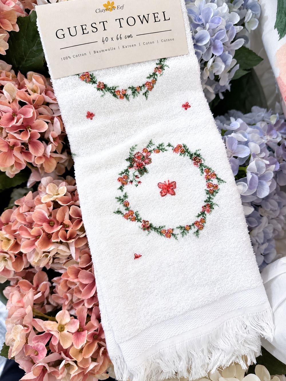Essuie-mains Couronne Florale avec ses franges, présenté parmi des hortensias roses et bleus.