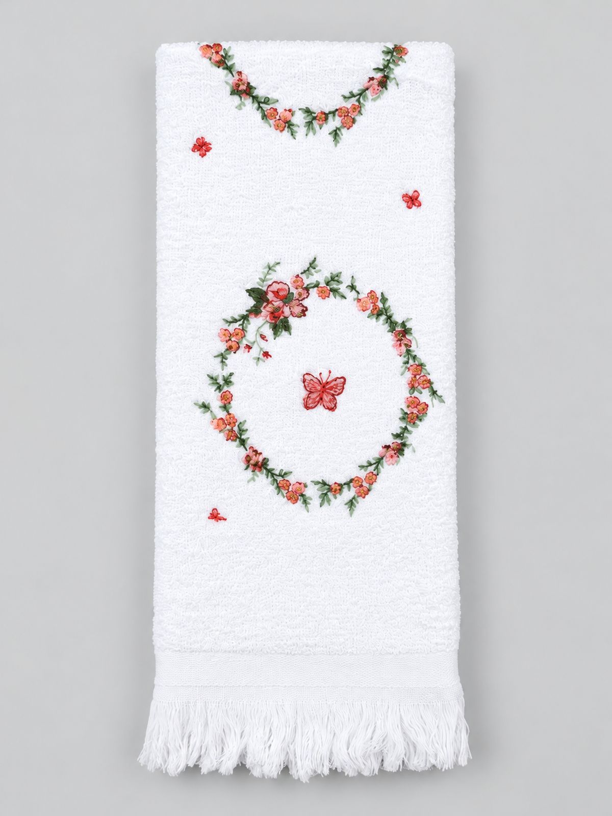 Essuie-mains blanc à couronnes florales roses et papillons, avec franges, présenté sur fond gris clair.