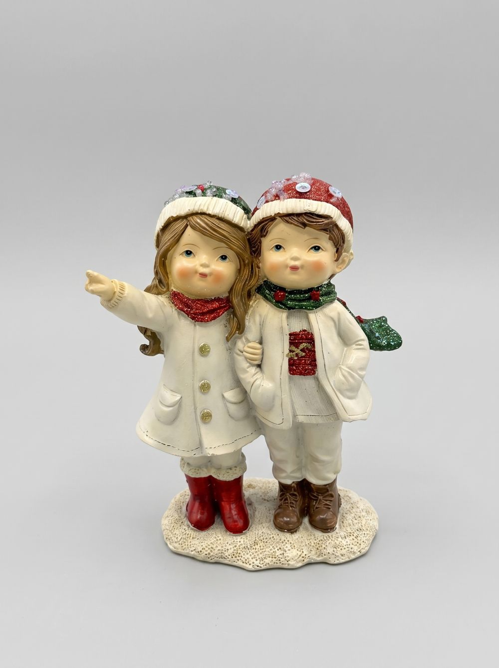 Figurine de Noël représentant deux enfants enlacés en tenue d’hiver, dans des tons blanc cassé, rouge et vert, idéale pour une décoration de Noël romantique et poétique