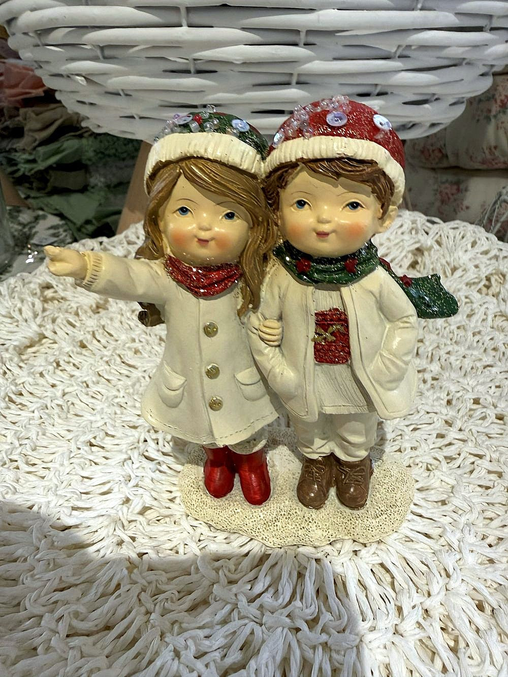 Figurine de Noël représentant deux enfants enlacés en tenue d’hiver, dans des tons blanc cassé, rouge et vert, idéale pour une décoration de Noël romantique et poétique