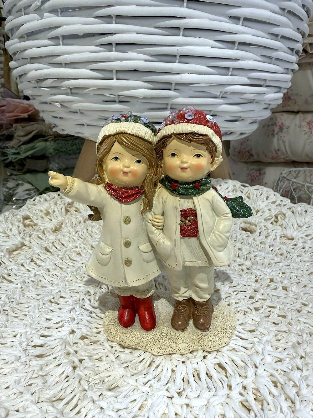 Figurine de Noël représentant deux enfants enlacés en tenue d’hiver, dans des tons blanc cassé, rouge et vert, idéale pour une décoration de Noël romantique et poétique
