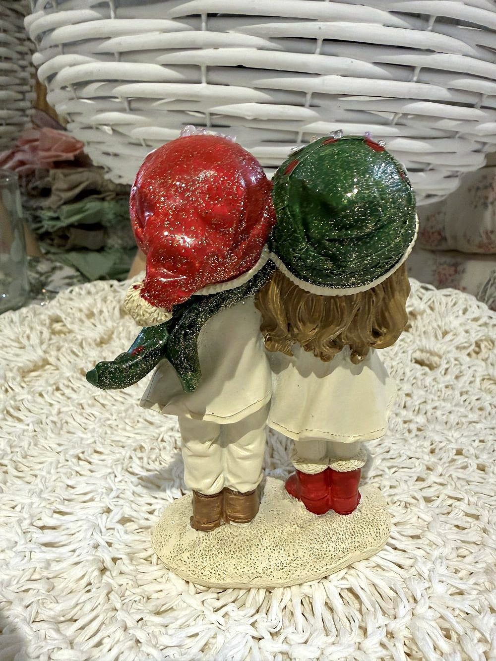 Figurine de Noël représentant deux enfants enlacés en tenue d’hiver, dans des tons blanc cassé, rouge et vert, idéale pour une décoration de Noël romantique et poétique