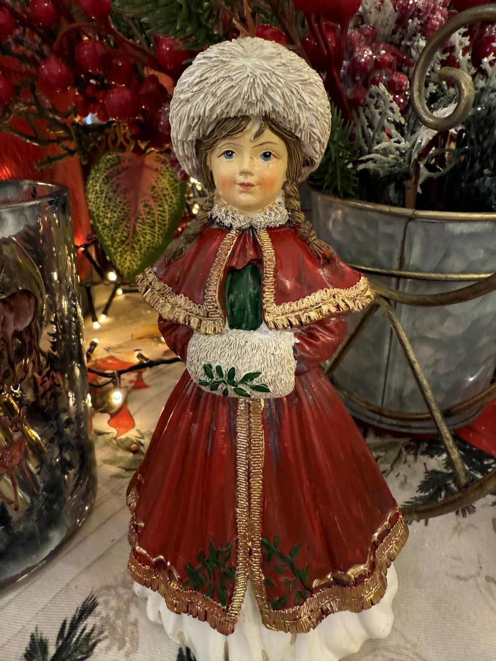 Figurine matriochka décorative en manteau rouge avec bonnet blanc, détails dorés et style hivernal féérique, posée dans une ambiance de Noël chaleureuse