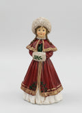Figurine matriochka décorative en manteau rouge avec bonnet blanc, détails dorés et style hivernal féérique, posée dans une ambiance de Noël chaleureuse