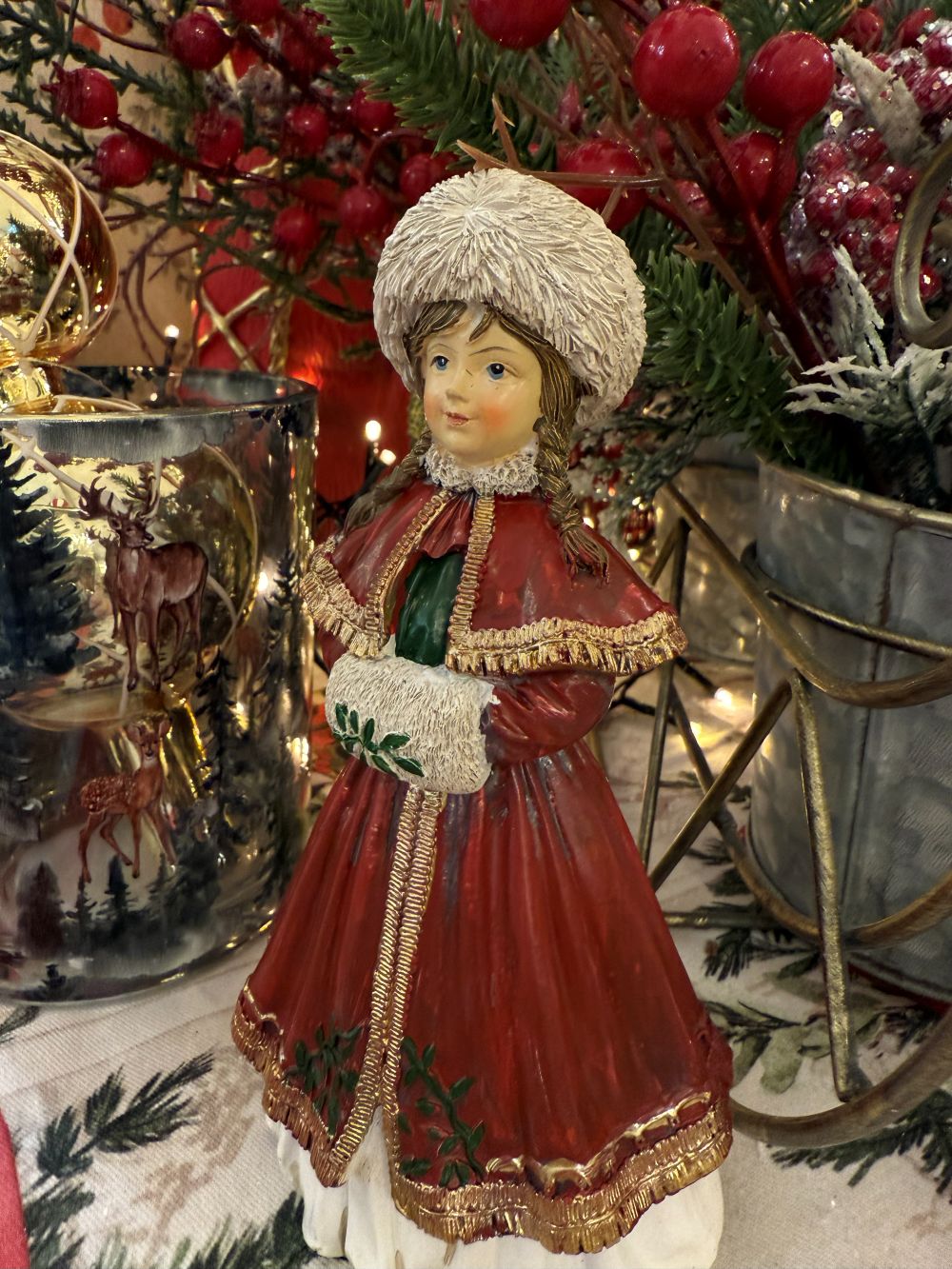 Figurine matriochka décorative en manteau rouge avec bonnet blanc, détails dorés et style hivernal féérique, posée dans une ambiance de Noël chaleureuse