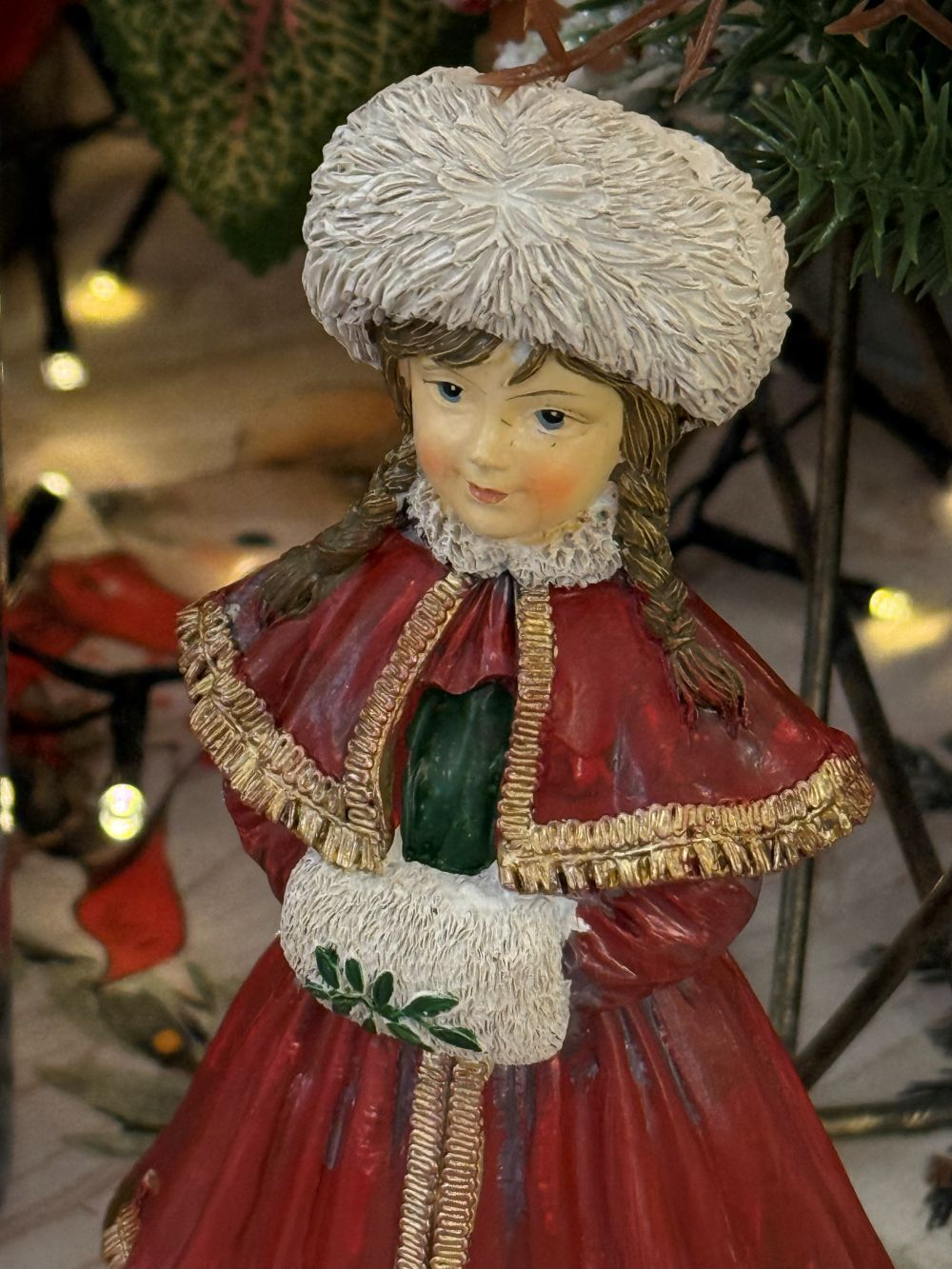 Figurine matriochka décorative en manteau rouge avec bonnet blanc, détails dorés et style hivernal féérique, posée dans une ambiance de Noël chaleureuse