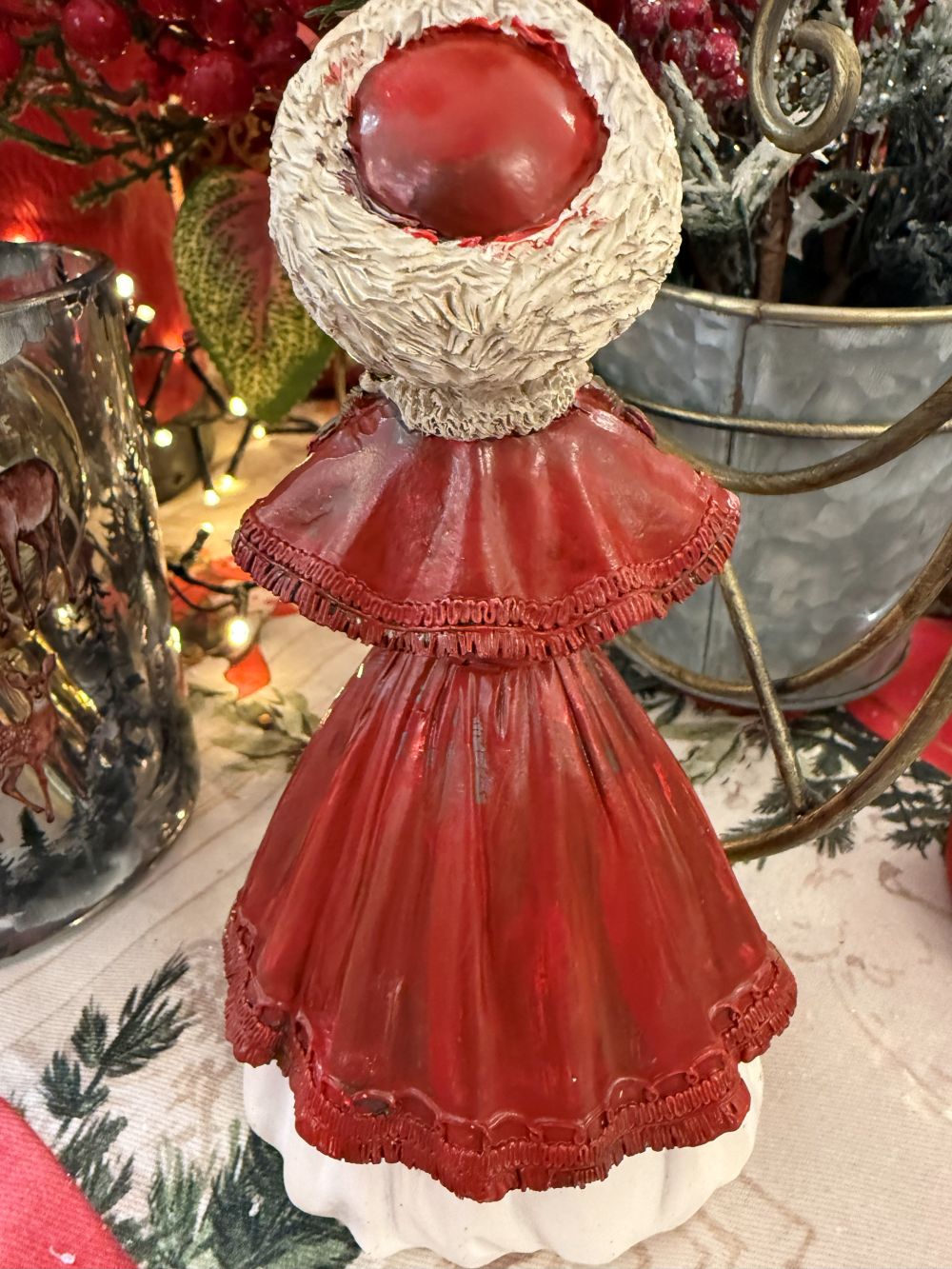 Figurine matriochka décorative en manteau rouge avec bonnet blanc, détails dorés et style hivernal féérique, posée dans une ambiance de Noël chaleureuse
