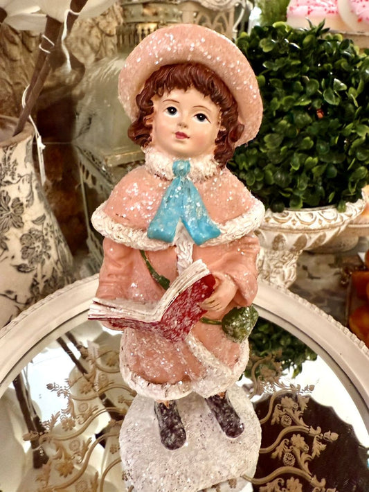 Figurine de Noël représentant une petite chanteuse en manteau rose et bonnet assorti, dans un style victorien romantique, sur fond de décoration shabby chic