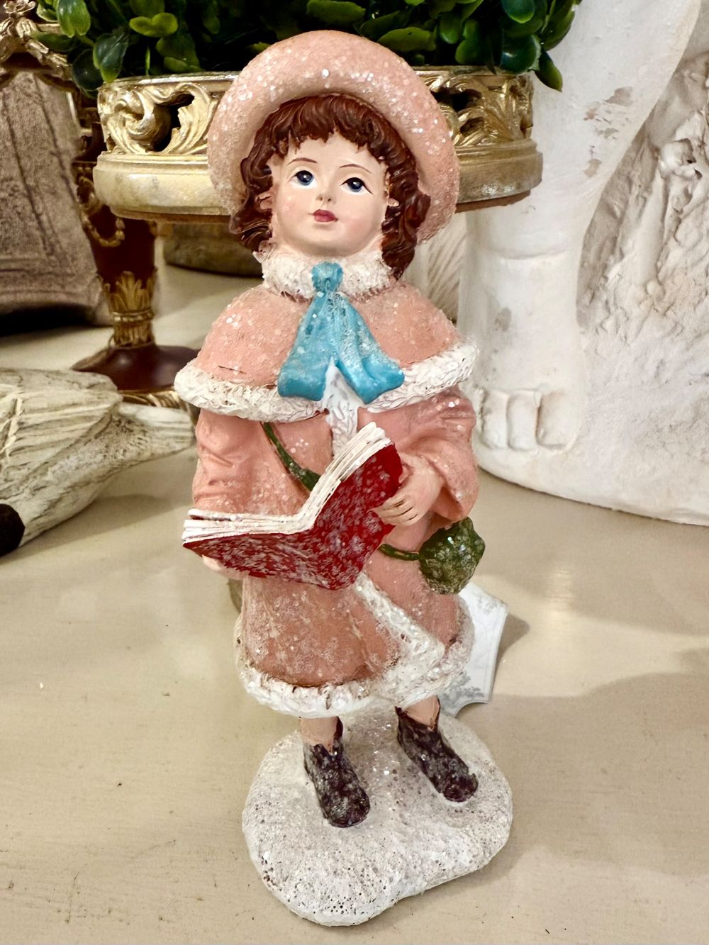 Figurine de Noël représentant une petite chanteuse en manteau rose et bonnet assorti, dans un style victorien romantique, sur fond de décoration shabby chic