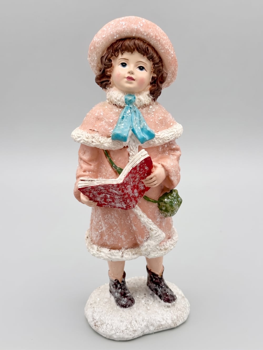 Figurine de Noël représentant une petite chanteuse en manteau rose et bonnet assorti, dans un style victorien romantique, sur fond de décoration shabby chic