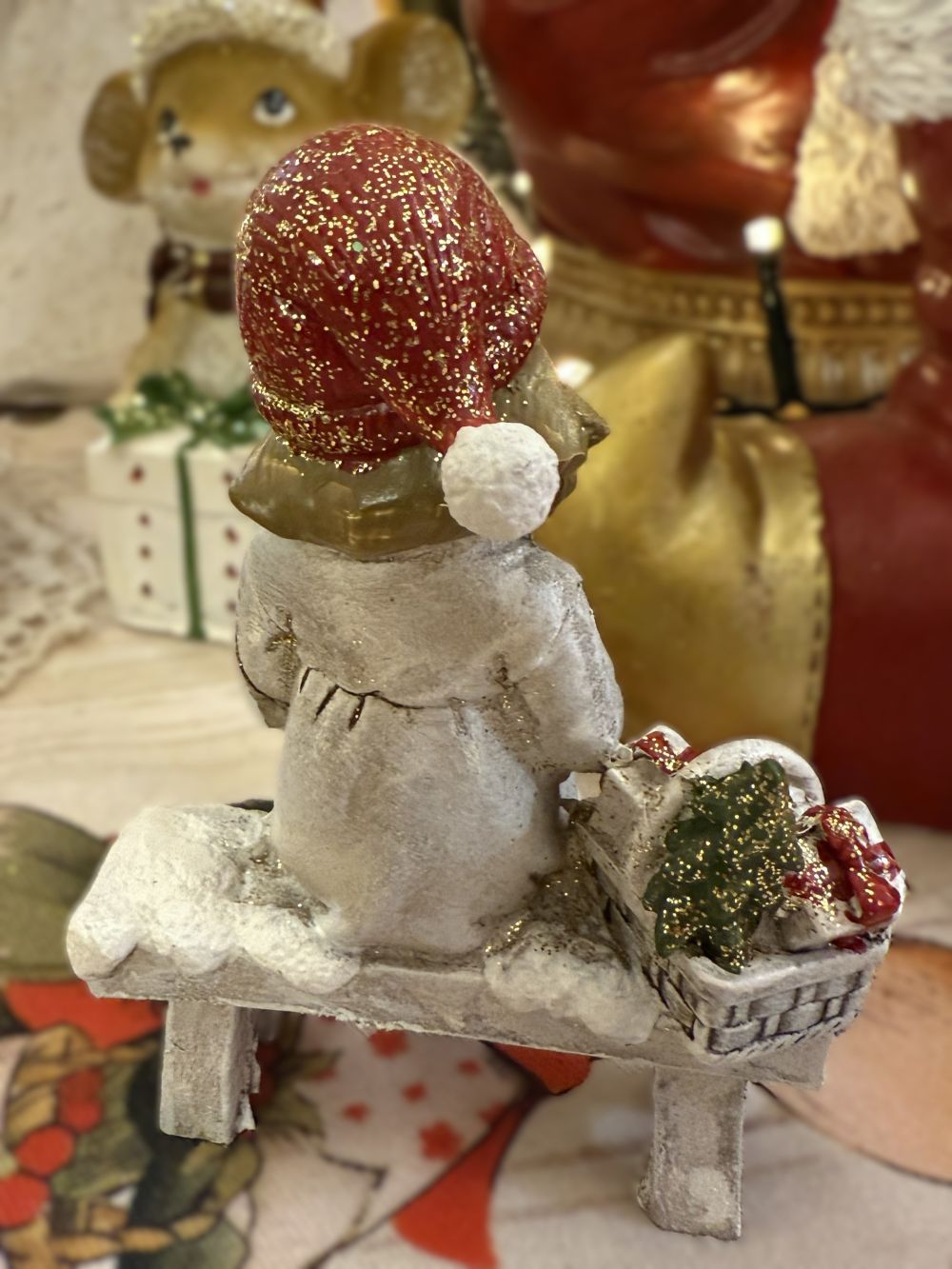 Figurine de Noël représentant une fillette assise sur un banc avec son petit chien blanc et un panier de cadeaux, couleurs blanc rouge et beige, style décoration romantique shabby chic et ambiance féérique