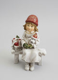 Figurine de Noël représentant une fillette assise sur un banc avec son petit chien blanc et un panier de cadeaux, couleurs blanc rouge et beige, style décoration romantique shabby chic et ambiance féérique