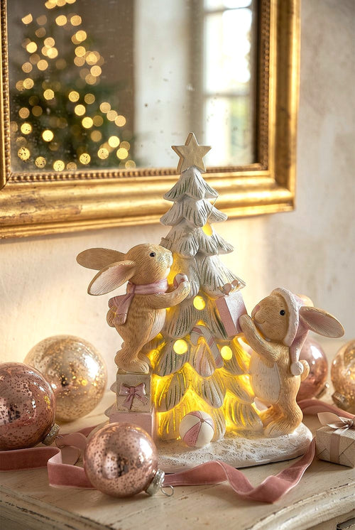 Figurine de Noël avec deux lapinous autour d’un sapin lumineux, tons vert givré, crème et rose poudré, décoration féérique et romantique
