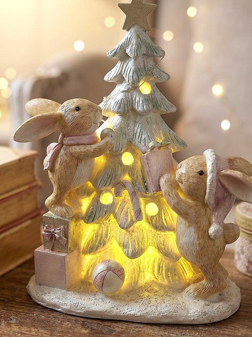 Figurine de Noël avec deux lapinous autour d’un sapin lumineux, tons vert givré, crème et rose poudré, décoration féérique et romantique