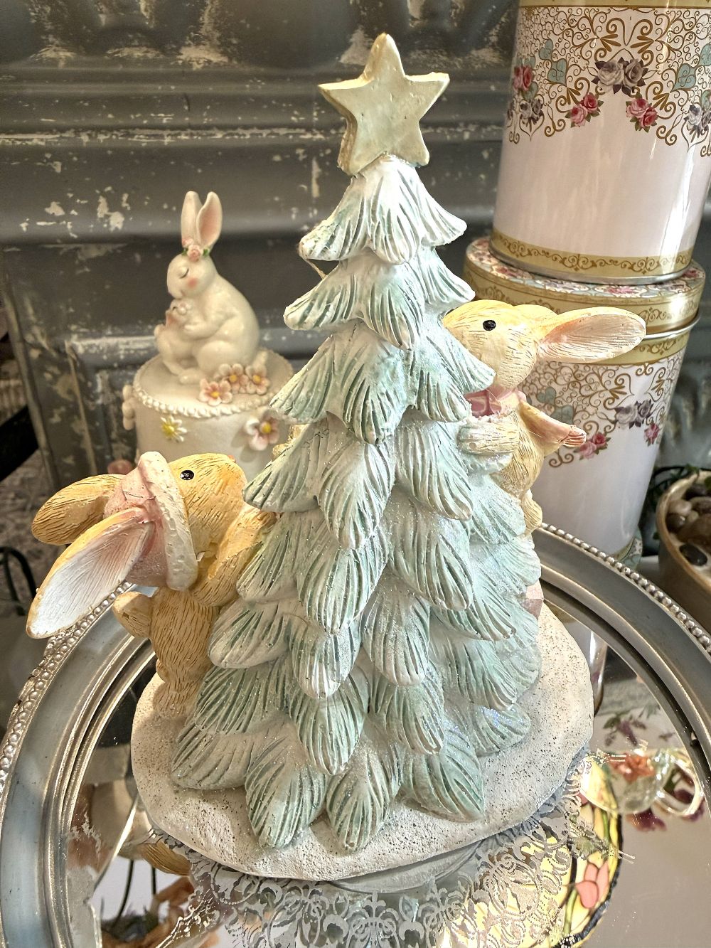 Figurine de Noël avec deux lapinous autour d’un sapin lumineux, tons vert givré, crème et rose poudré, décoration féérique et romantique