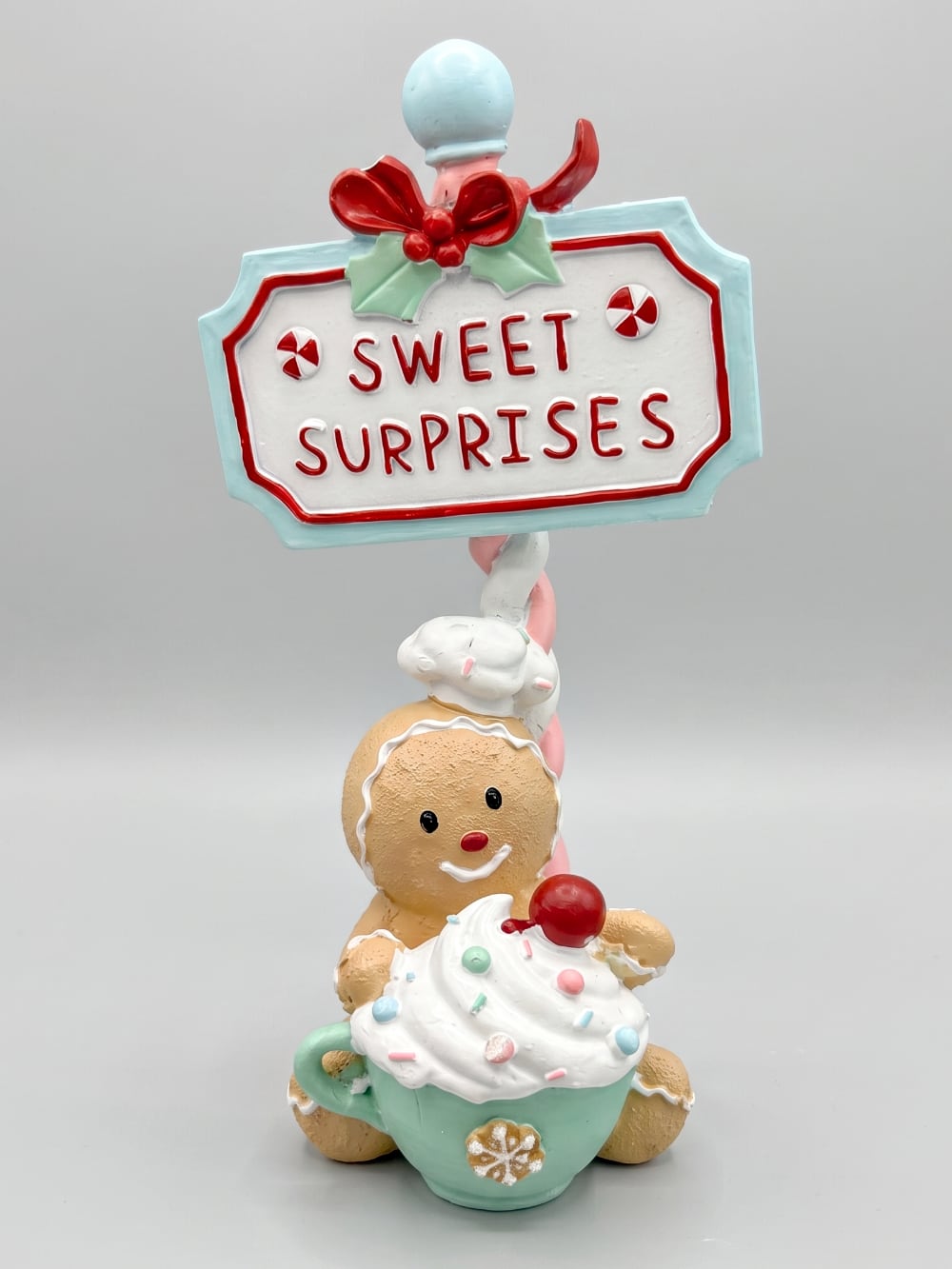 Figurine de Noël Sweet Surprise avec personnage biscuit, cupcake, enseigne rétro, teintes caramel, bleu pastel et rouge dans une ambiance gourmande et féérique
