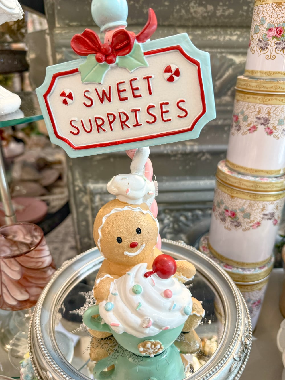 Figurine de Noël Sweet Surprise avec personnage biscuit, cupcake, enseigne rétro, teintes caramel, bleu pastel et rouge dans une ambiance gourmande et féérique