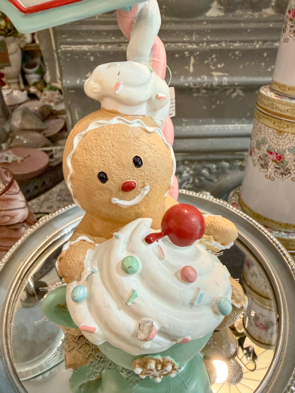 Figurine de Noël Sweet Surprise avec personnage biscuit, cupcake, enseigne rétro, teintes caramel, bleu pastel et rouge dans une ambiance gourmande et féérique