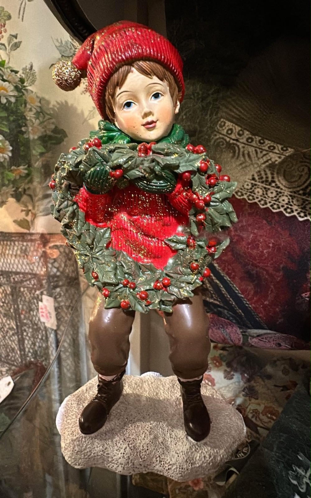 Figurine petit garçon de Noël en rouge et vert tenant une couronne végétale à baies rouges, décoration de Noël poétique et féérique