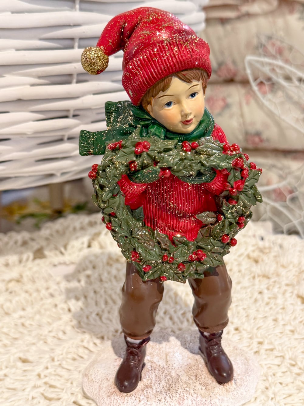 Figurine petit garçon de Noël en rouge et vert tenant une couronne végétale à baies rouges, décoration de Noël poétique et féérique